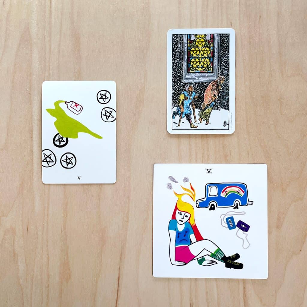 A photo of the Five of Pentacles from the Laughing Eye Weeping Eye tarot, Rider-waite tarot, and Colorful tears tarot. 